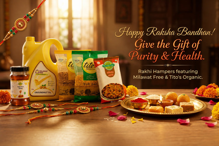 A festive Rakhi bandhan product display on a wooden table with a warm indoor background. Visible products include a yellow groundnut oil jug, a jar of chutney, bags of Tito's Organic milawal-free and organic snacks, and a tray of sweets and flowers.