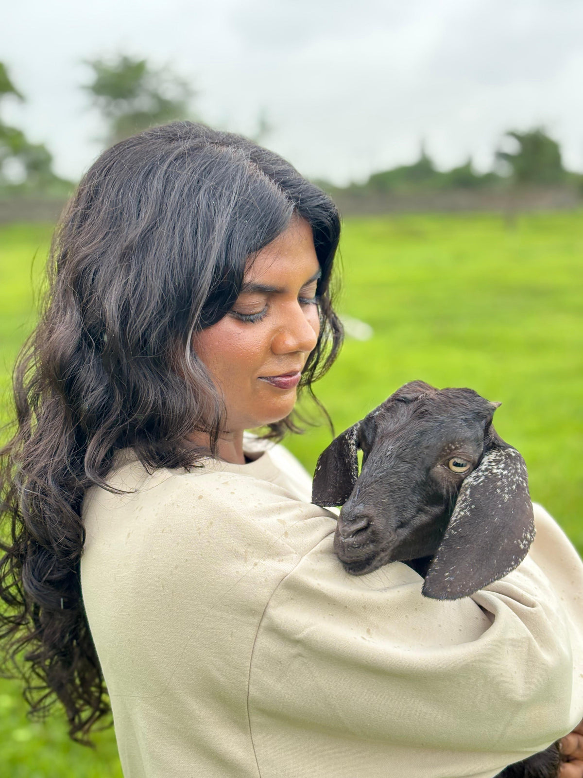 Reah Eve Daniel, CEO of Milawat Free, gently holding a baby goat in a lush green rural setting